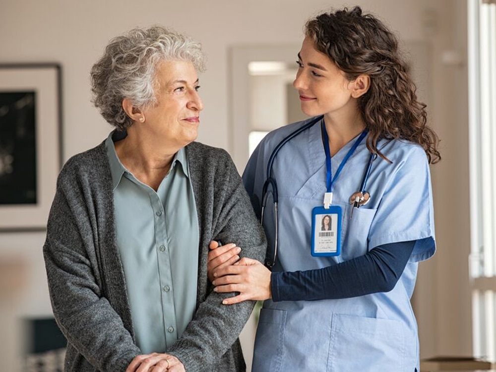 A nurse walks with a patient while holding her arm.
